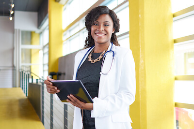 Portrait of a female doctor holding her patient chart on digital tablet in bright modern hospital